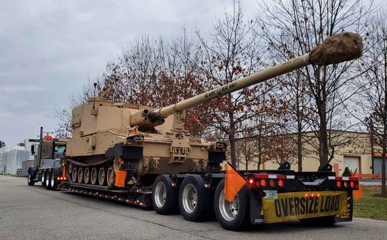 Trailer carrying XM1299 self-propelled artillery for road mobility. 